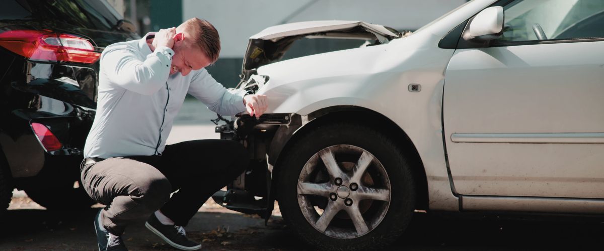 A man at the scene of a car accident who is holding his neck in pain, perhaps due to a whiplash injury.