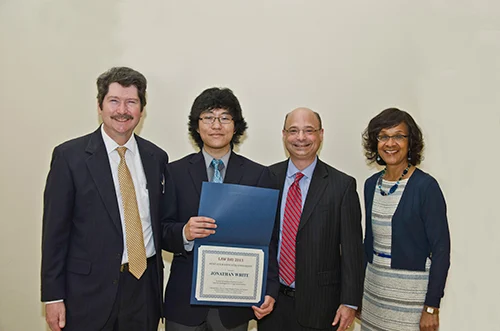 Group photo of three smiling professional adults, one holding an award certificate, likely at a legal event or ceremony.