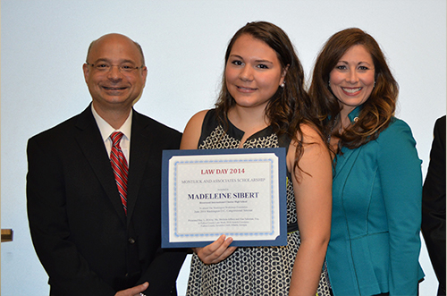Teen girl holds law day award certificate flanked by smiling man in suit and woman in teal blouse.