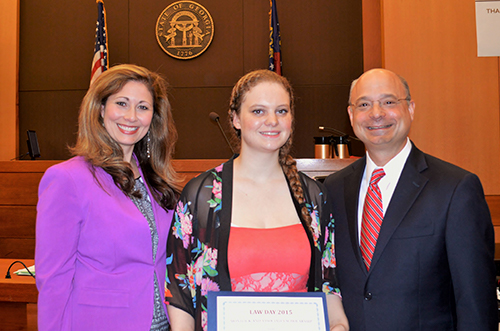 Attorney duo with award recipient at professional legal event, smiling in front of emblems
