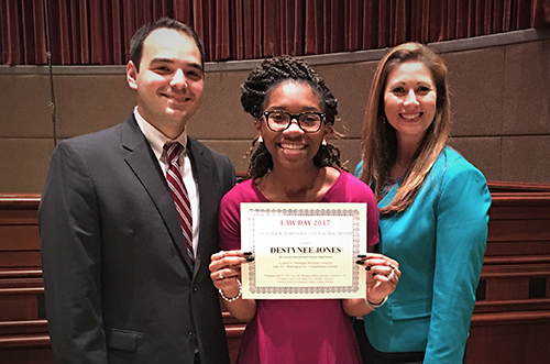 Student holding "Best All Around" award certificate flanked by smiling man in suit and woman in blue jacket
