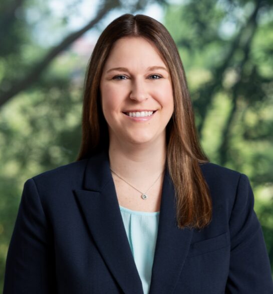Young smiling professional woman in suit jacket outdoors, warm welcoming expression, legal services