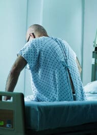 Rear view of patient in hospital gown sitting on bed, suggesting medical malpractice or injury case.