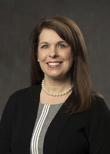 Smiling brunette female attorney wearing pearl necklace and black blazer, professional headshot