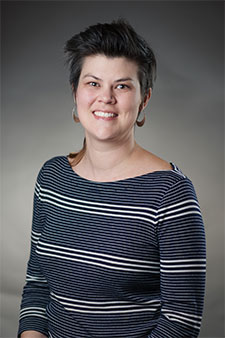 Smiling woman with short dark hair wearing a striped shirt, headshot on gray background.