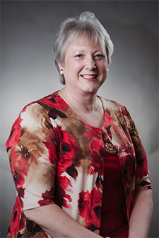 Smiling senior woman in red floral blouse on gray backdrop, representing clients helped by injury lawyer.