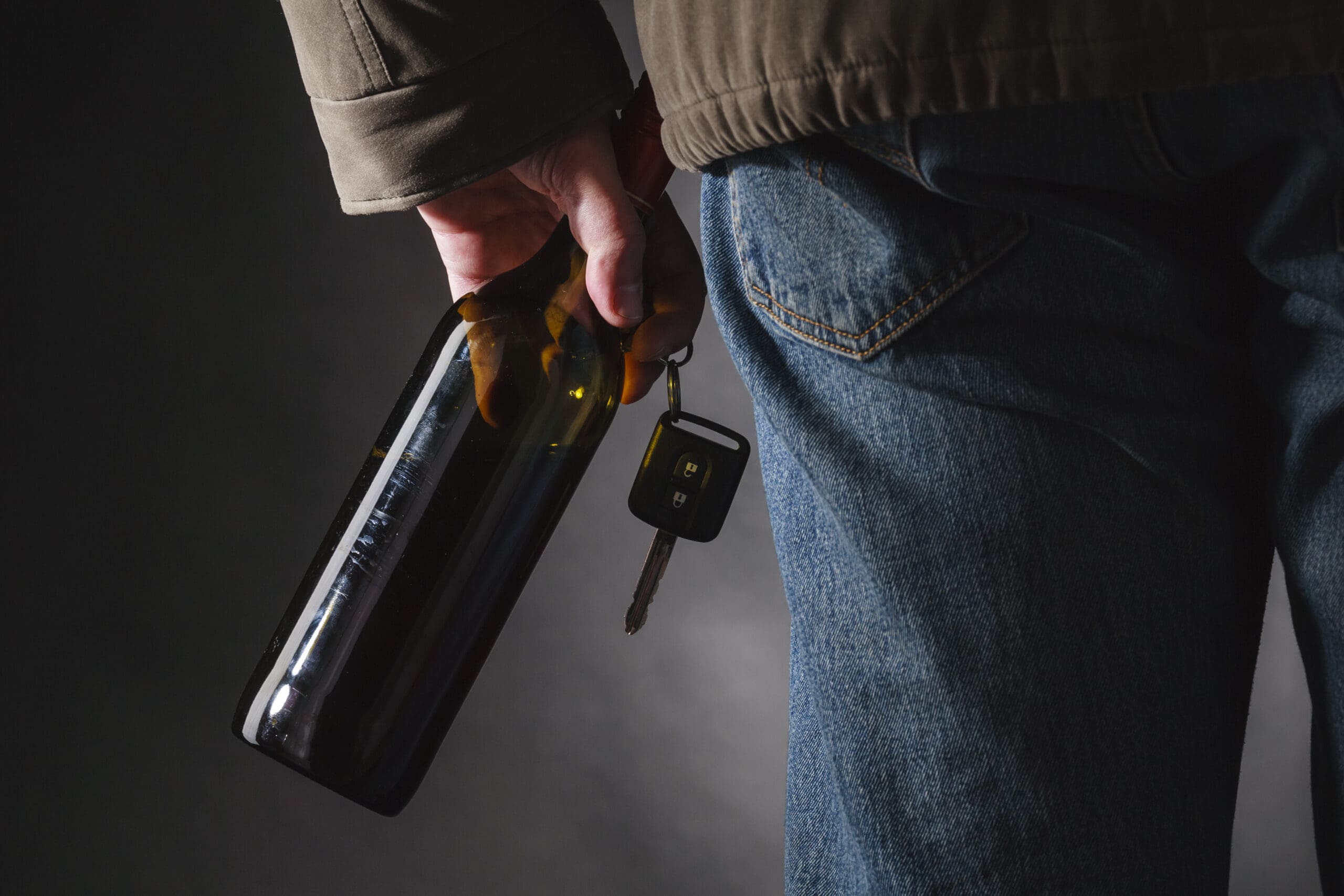 Man holding car keys with alcohol bottle, depicting drunk driving dangers - legal representation image.