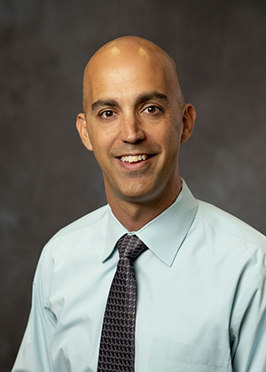 Smiling bald man in dress shirt and tie, professional headshot for attorney website, approachable look.
