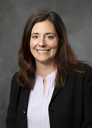 Professional headshot of smiling female attorney wearing a black blazer against a gray background.