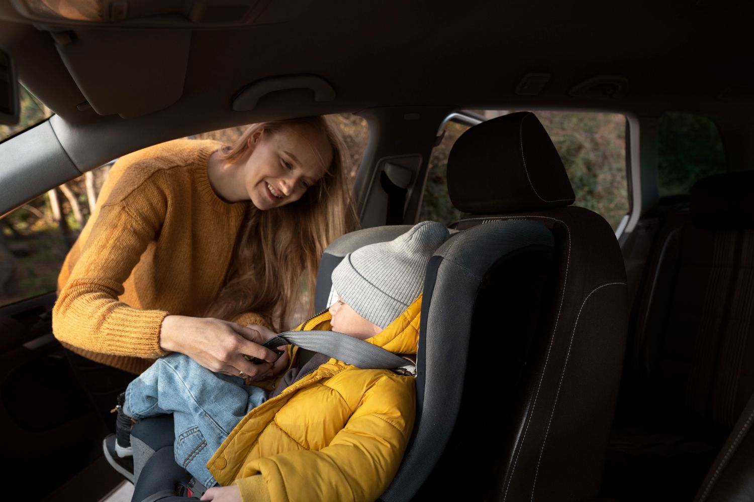 Young girl in car seat buckled up, smiling while looking at phone, promoting child car safety