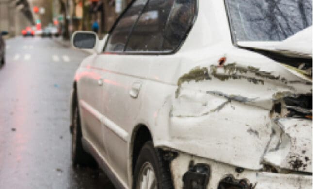 Damaged car on city street after accident, crumpled front end and missing headlight, injury attorney aid