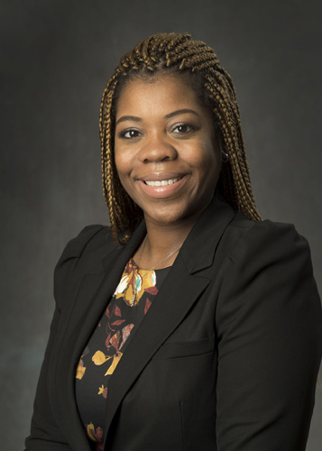 Smiling African American female attorney with braided hair wearing floral blouse and black blazer, professional headshot