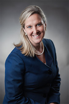 Smiling blonde female attorney wearing blue blouse, professional headshot on gray background