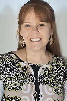 Smiling woman with long brown hair wearing black and white patterned shirt and dangling earrings.