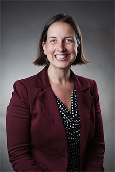 Professional headshot of smiling female attorney wearing burgundy blazer on gray background
