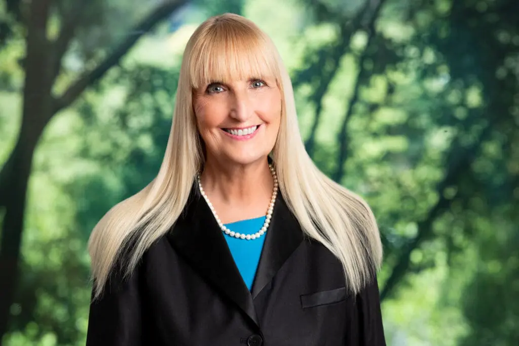 Smiling blonde woman lawyer wearing pearl necklace and black suit jacket with vibrant green background