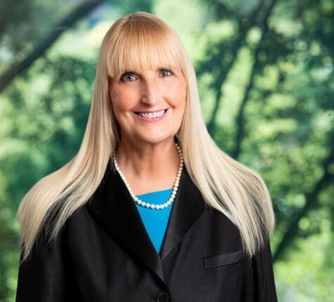 Smiling blonde woman lawyer wearing pearl necklace and black suit jacket with vibrant green background