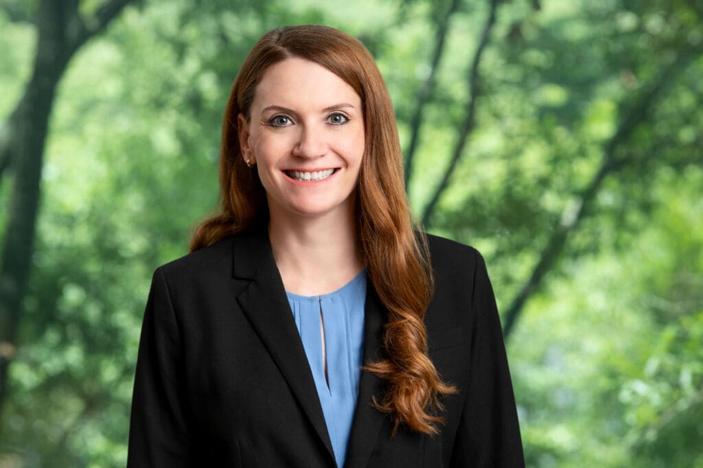 Smiling female lawyer with long brown hair wearing a black suit jacket, ready to assist clients.