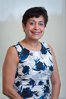 Smiling brunette woman wearing floral dress on plain background, looking friendly and approachable.
