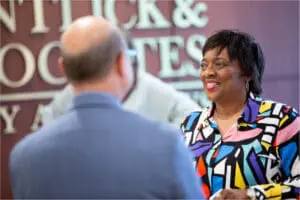 Three smiling women in blue tops talking at an office event, appearing friendly and professional.