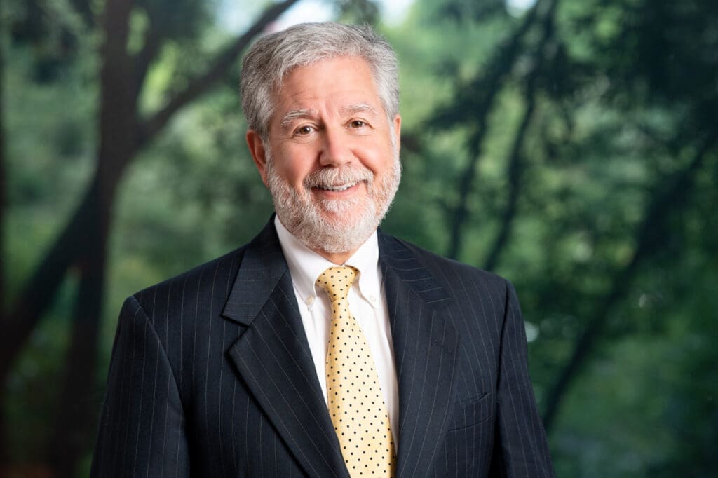 Smiling senior attorney in suit and tie standing outdoors, ready to help with legal matters.