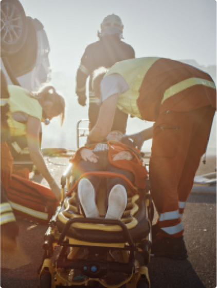 EMTs treating injured victim on stretcher at accident scene in bright sunlight, close-up view.