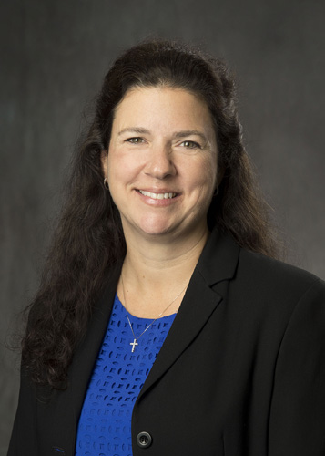 Professional headshot of smiling female attorney wearing blue blouse and black blazer on gray background