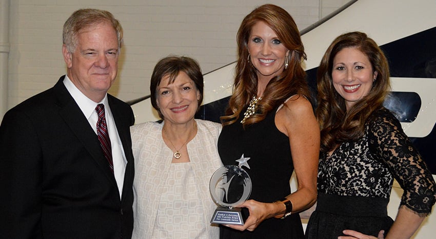 Group portrait of an attorney with three smiling clients holding an award, promoting legal services.