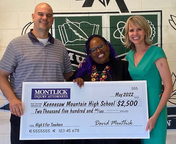 Injury attorney presents $2,500 donation check to smiling Kennesaw Mountain High School teachers.