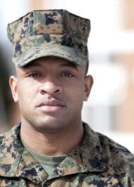 Young serious-faced male soldier in camo uniform cap, looking straight ahead. Closeup headshot photo.