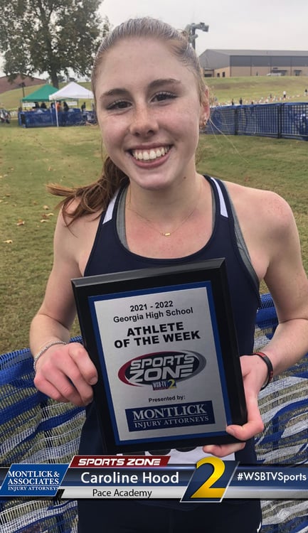 Smiling high school athlete holding an Athlete of the Week award plaque at an outdoor sporting event.