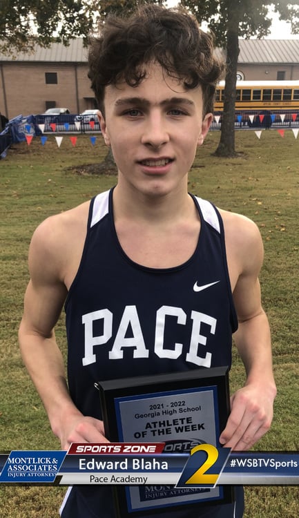 Young male athlete holding "Athlete of the Week" award, wearing Pace Academy sports jersey, outdoors on grass field.