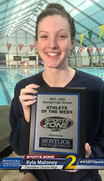 Smiling high school athlete of the week holding award plaque at indoor pool, presented by injury attorneys