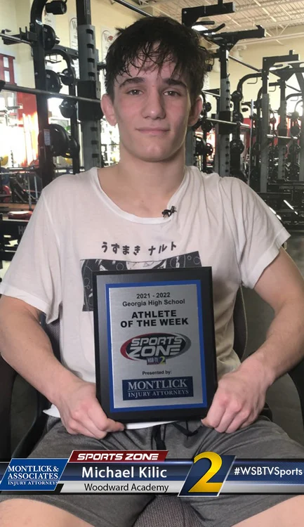 High school athlete holding "Athlete of the Week" award inside a workout facility with exercise equipment.