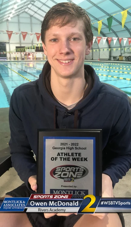 Athlete of the Week Owen McDonald smiling while holding Sports Zone award in a swimming pool facility.