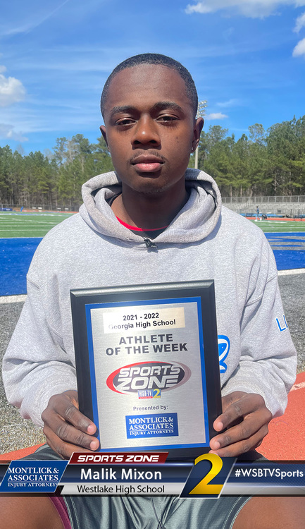 High school athlete of the week holds award plaque on sports field, smiling at camera.