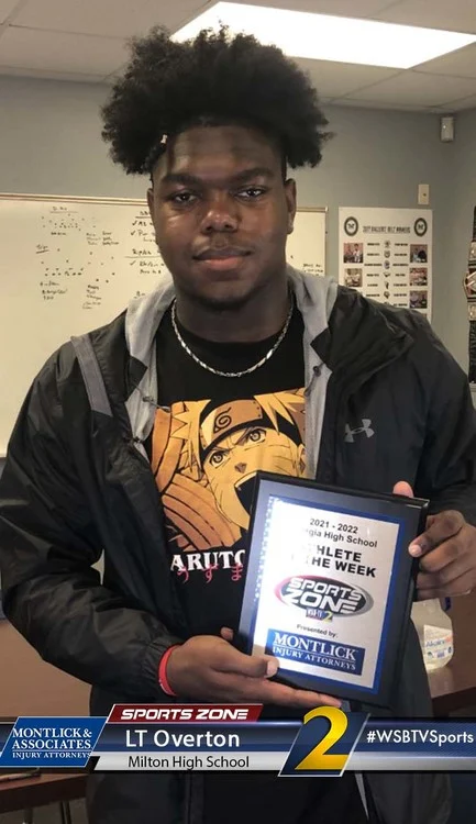 African American high school student athlete holding certificate, notepad and coffee mug in classroom setting