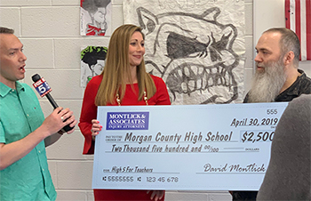 Morgan County High School teacher receives $2,500 donation check presented by two men on either side.