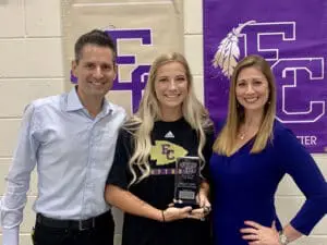 Friendly sports injury attorney standing with smiling female athlete holding award, in front of FC logo banner.