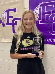 Smiling female softball player holding award in front of EFC Softball Outreach banner. Athletic injury lawyer.