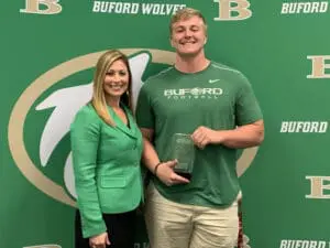 Buford football player holding sports award poses with woman in front of team banner, smiling