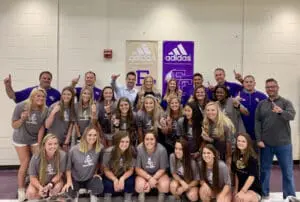 Group photo of high school volleyball team posing in front of Adidas banner, players and coaches smiling