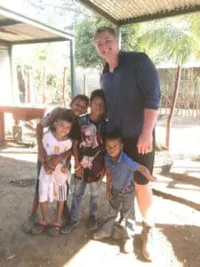 Smiling man with four young children in rural outdoor setting - family, community, compassion