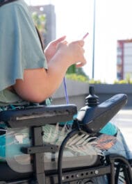 Man in power wheelchair using smartphone outdoors, representing mobility and accessibility rights.