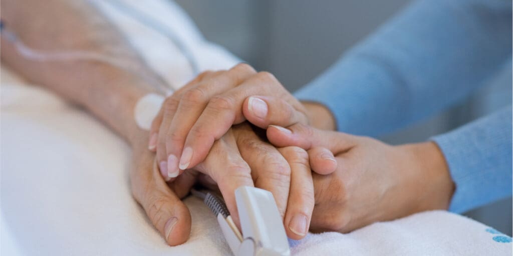 Caring hands holding patient's hand in hospital, offering support and comfort during recovery.