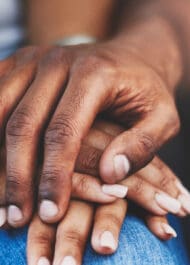 Black woman's hands clasped, showing nails, on blue denim jeans. Personal injury concept image.