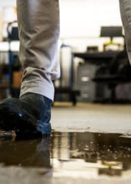 Person walking on wet floor near spill, risking slip and fall injury at workplace or business