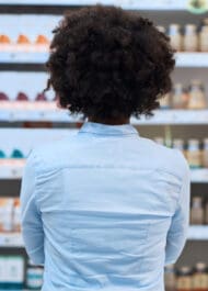 Young woman with curly hair examining supplements in a health food store. Rear view.