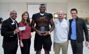 High school football player receives community service award, joined by supportive school staff.