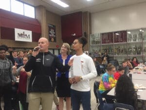 Coach speaking to high school students in a school cafeteria about athletics, character and education.
